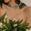 Woman holding white tulips wearing a turquoise beaded necklace against a neutral background, light blue beaded turquoise necklace
