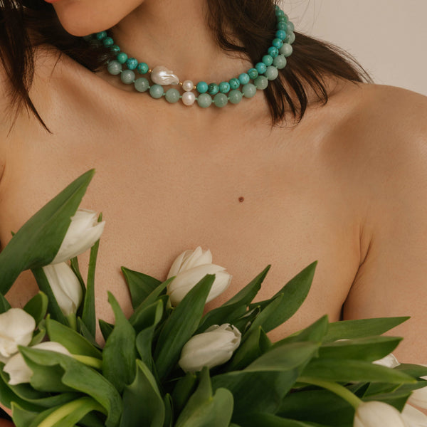 Woman holding white tulips wearing a turquoise beaded necklace against a neutral background, light blue beaded turquoise necklace