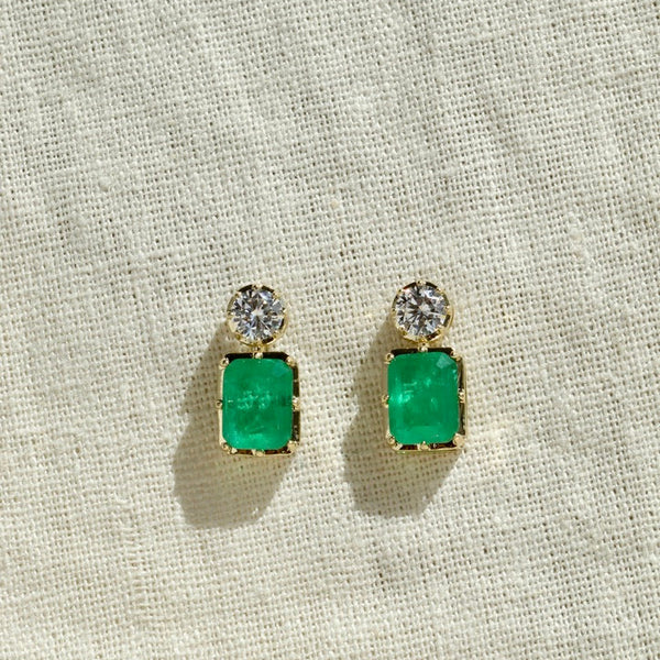 Pair of emerald green square earrings with clear stones on a beige fabric background