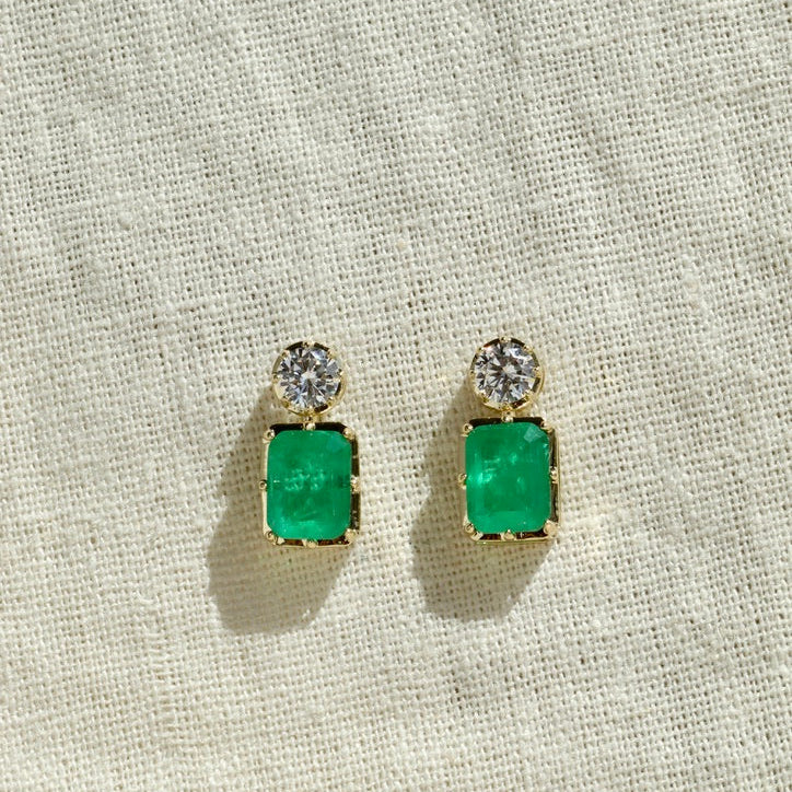 Pair of emerald green square earrings with clear stones on a beige fabric background