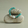 Turquoise beaded bracelet with a white pearl on a stack of stones against a beige background