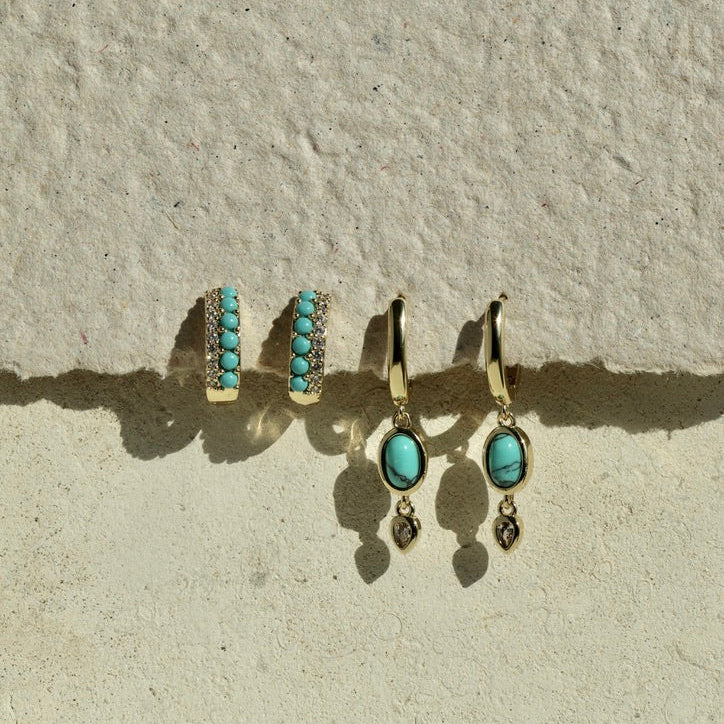 Turquoise earrings on a textured beige surface