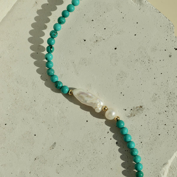 Turquoise beaded necklace with white pearls on a textured surface